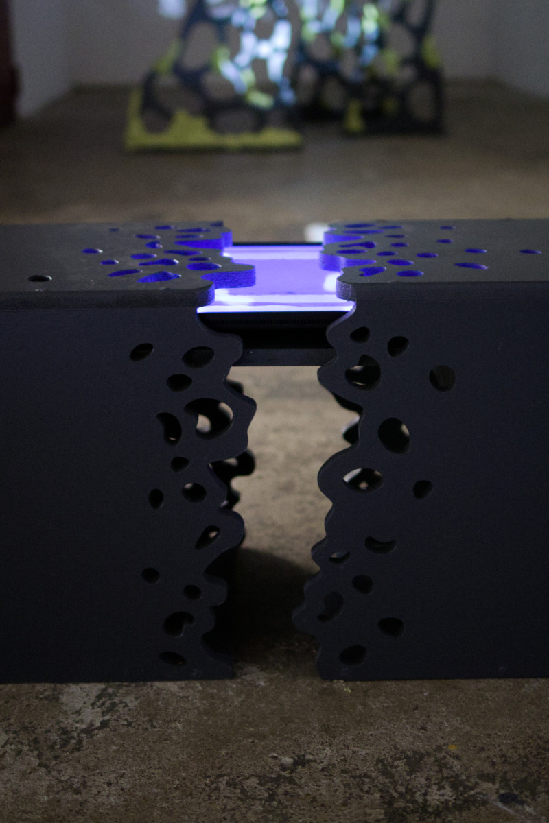 banc noir sculpté dans lequel se trouve un écran projetant des images 3D blueues