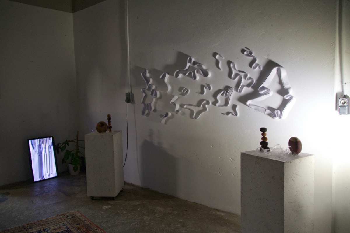 vue d'ensemble de la sculpture de papier entourée de socles présentant des objets en bois et plexiglas et un écran