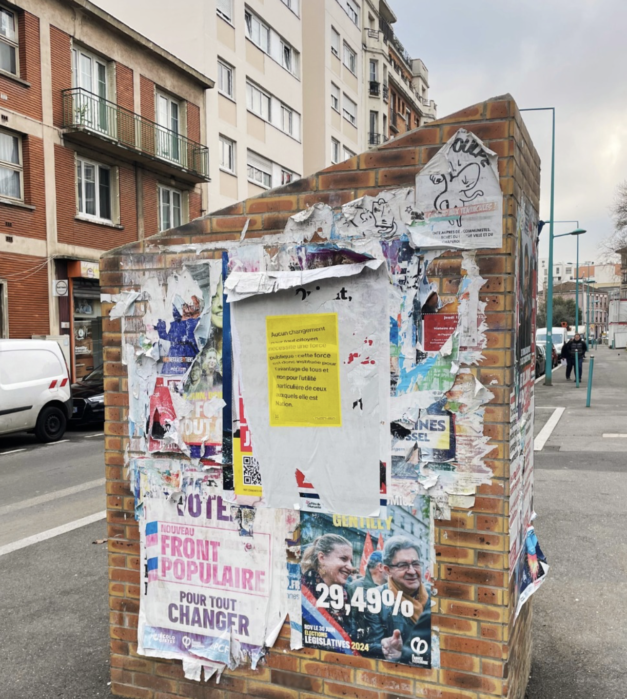 photographie de rue de Gentilly où une affiche jaune comprenant un poème constitutionnel d'antonin jousse est accrochée sur un espace publicitaire au-dessus d'affiches politiques